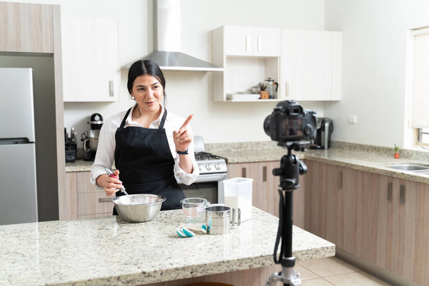 Attraktive junge weibliche Influencerin, die während der Zubereitung von Kuchen in der Küche Vlog durch die Kamera macht - Foto, Bild