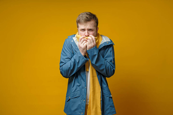 Man feels sick, he has a fever, he covers mouth with a scarf and is afraid of a dangerous virus, on a yellow background. - Fotografie, Obrázek