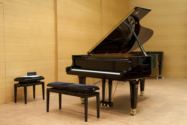 Un piano negro listo para tocar con taburete delante en un escenario de madera
 - Foto, imagen