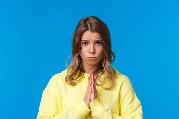 Close-up portrait of cute sulky european female blonde begging for help, asking favour, really need something, holding hands in pray, frowing and sobbing as plead for apology, blue background - Photo, Image