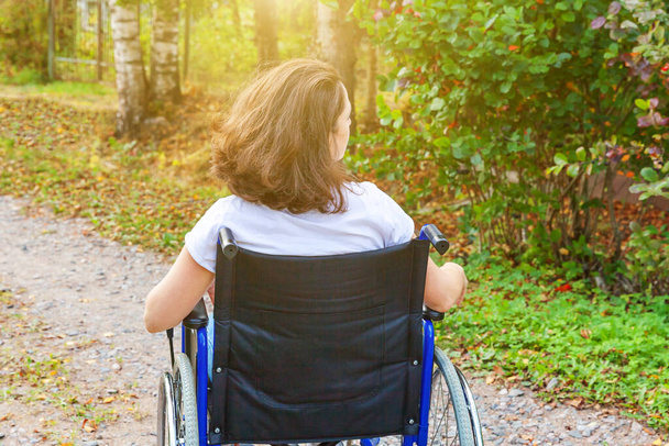 病院公園の路上で車椅子の若い幸せなハンディキャップの女性は自由を楽しんでいます。自然の中で屋外の障害者のための無効な椅子に麻痺した女の子.リハビリテーションの概念 - 写真・画像