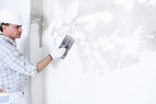 sádrokarton muž při práci s lopatkou omítání stěny interiéru staveniště nosit přilbu a ochranné rukavice, izolované a kopírovat prostor na bílé stěně - Fotografie, Obrázek