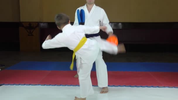 Ein Athlet schlägt einen Tritt mit einem Arm und einem Fuß auf einem orangefarbenen Ball und einem blauen Simulator - Filmmaterial, Video