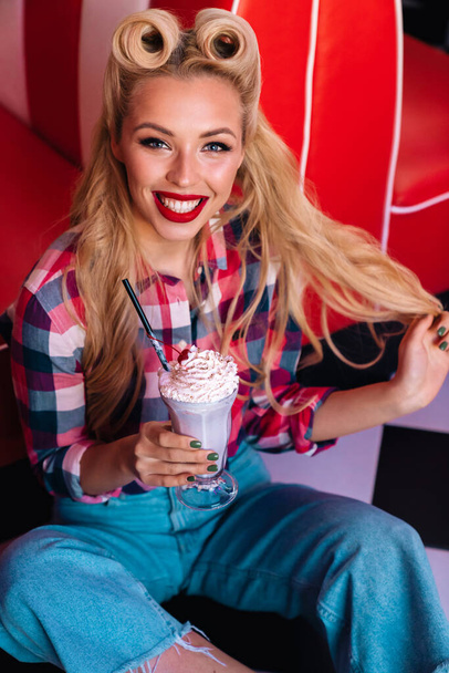 Photo of gorgeous cheerful woman with beautiful hairstyle drinking milkshake in retro american cafe - Foto, Bild