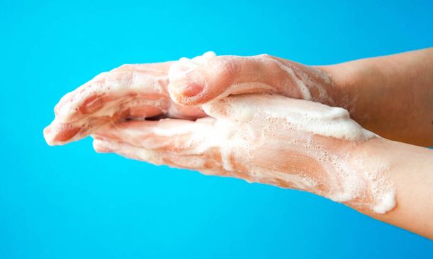 Kobiece ręce trzymają mydło. Pianka mydlana na dłoniach. Żółte mydło w dłoniach. Kobieta myje mydło z bocznym widokiem na niebieskie tło. Ochrona przed wirusami. COVID-19 - Zdjęcie, obraz