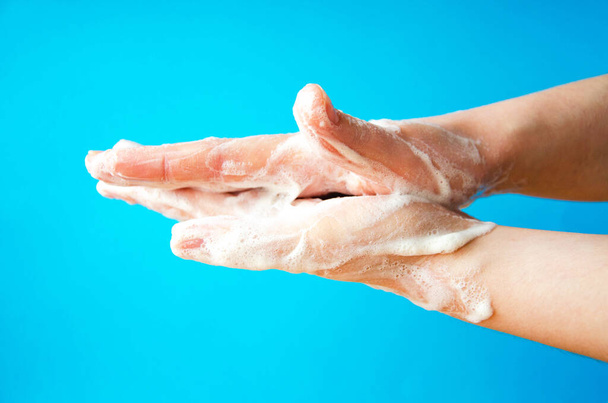 As mãos das mulheres estão a segurar sabão. Espuma de sabão nas mãos. Sabão amarelo nas mãos. Mulher lava sabão com as mãos vista lateral sobre um fundo azul. Proteção de vírus. COVID-19
 - Foto, Imagem