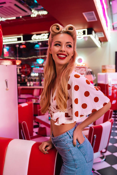 Photo of cheerful caucasian woman with beautiful hairstyle posing and smiling at camera in retro american cafe - Foto, Imagen