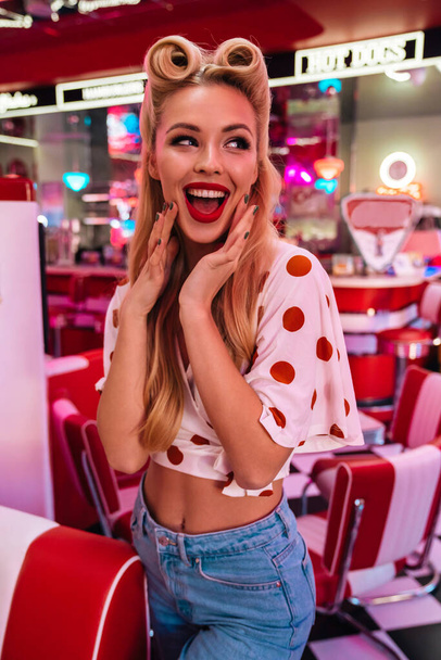 Photo of cheerful caucasian woman with beautiful hairstyle posing and smiling at camera in retro american cafe - Foto, Bild