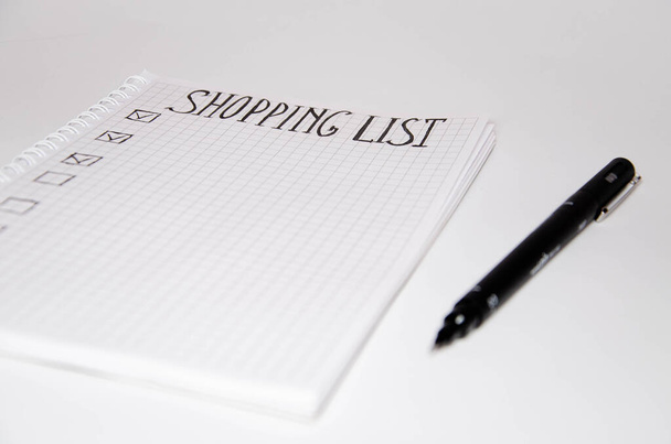 買い物リスト。白い背景に黒いペンの付いた正方形のノートブック。アイデア、メモ、計画、タスクを記録します。リストにはパン、牛乳、バナナが含まれています。コピースペース - 写真・画像