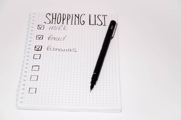 Lista de compras. Cuadrado cuaderno con bolígrafo negro sobre un fondo blanco. Graba ideas, notas, planes, tareas. La lista incluye pan, leche, plátanos. Copia Spase
 - Foto, Imagen