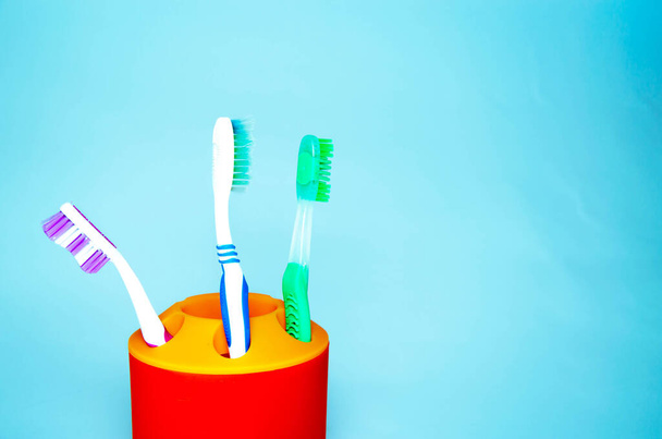 Três escovas para limpar dentes em um vidro branco e laranja em um fundo azul. Máquinas de barbear em um copo. Escovas e máquinas-ferramentas em um vidro em um fundo azul. Espaço de cópia
 - Foto, Imagem