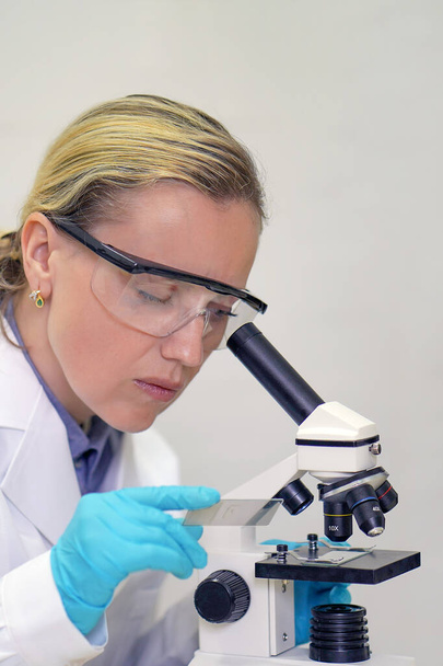 Substâncias bioquímicas femininas misturando para estudar ao microscópio. Estudante de ciências a ver o microscópio no laboratório da universidade. Técnico em laboratório usando um microscópio
. - Foto, Imagem
