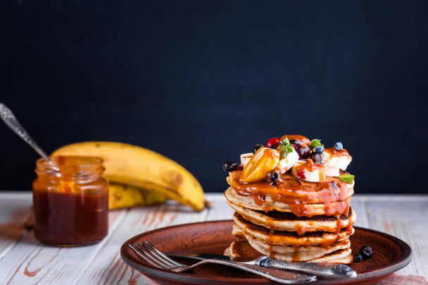 Вкусные блины с бананом, ягодами, мятой и соленой карамелью в тарелке. Вкусный завтрак
 - Фото, изображение