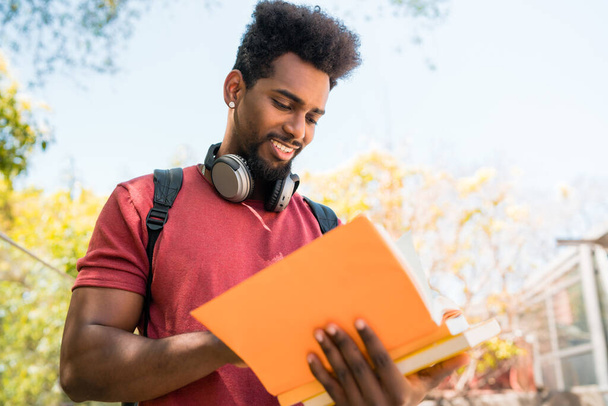 Retrato do jovem estudante afro-universitário lendo e estudando com seu livro no campus. Educação e conceito de estilo de vida. - Foto, Imagem