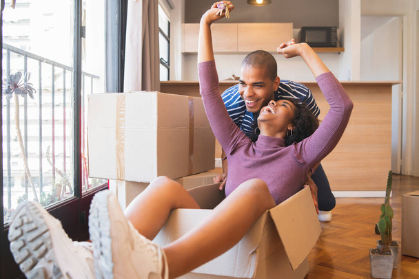Portrait of happy latin couple having fun with cardboard boxes in new house at moving day. Real estate concept. - Photo, image