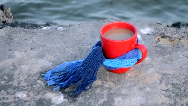 Czerwony kubek z gorącą herbatą i parą, związany z niebieską dzianiną szalik - Materiał filmowy, wideo