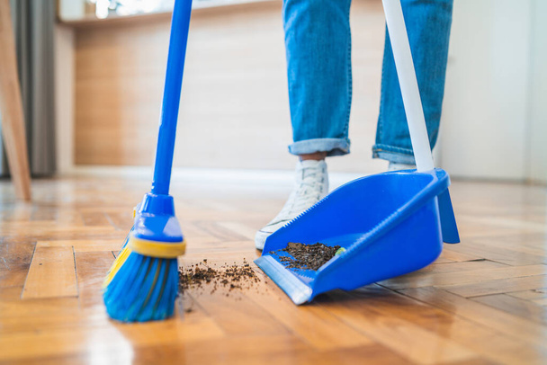 Portrait of young latin man sweeping wooden floor with broom at home. Cleaning, housework and housekeeping concept. - 写真・画像