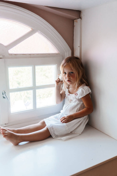 beautiful girl in white dress sitting on the windowsill  - Foto, imagen