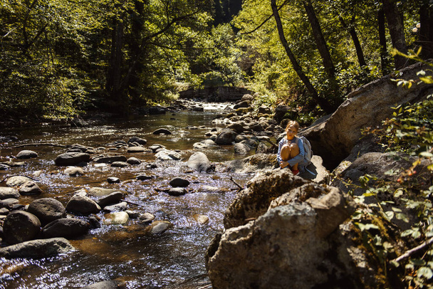 young girl with backpack sitting near rapid river   - Fotoğraf, Görsel