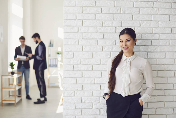 Hispanic latin business woman smiling while standing in a white office against a white wall. - 写真・画像