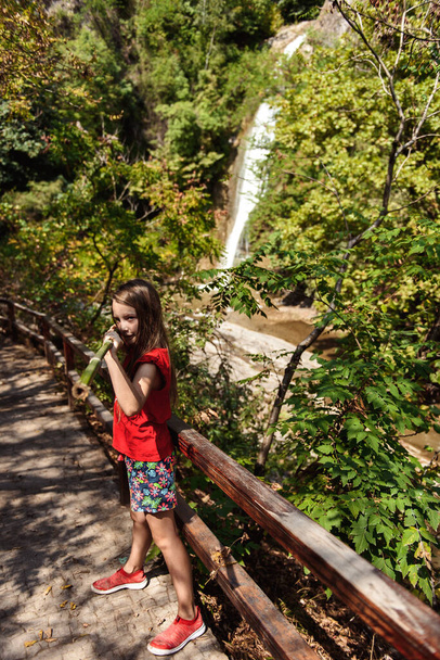 beautiful young girl standing near waterfall in forest. - Foto, afbeelding