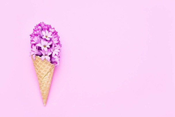 Waffle ice cream cone with pink hyacinth flower on pink background. Spring concept. Copy space for text, top view - Photo, Image