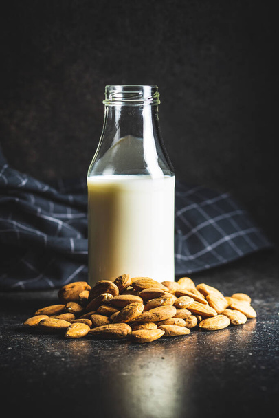 Almonds nuts and almond milk in bottle on black kitchen table. - Zdjęcie, obraz