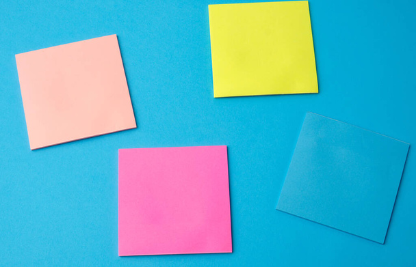 pegatinas de papel en blanco multicolor de diferentes colores sobre un fondo azul, espacio de copia
 - Foto, Imagen