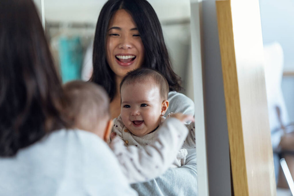 Shot of happy young mother with her little girl looking in the mirror while smiling at home. - Фото, изображение
