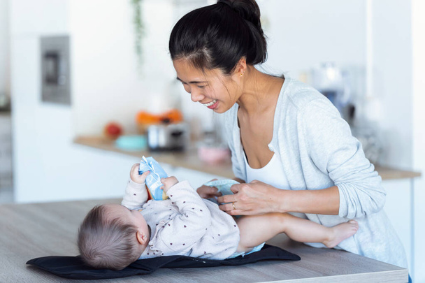 Tiro de sorrir jovem mãe se diverte com o bebê enquanto troca sua fralda em casa
. - Foto, Imagem