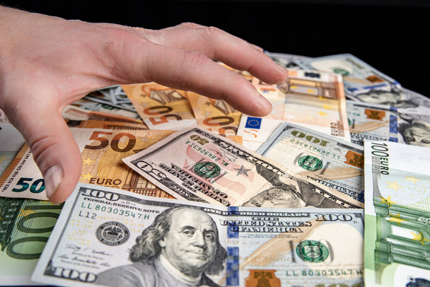 Hand over american dollars and euro lying randomly on black background. Concept, cash, wealth - Foto, Bild