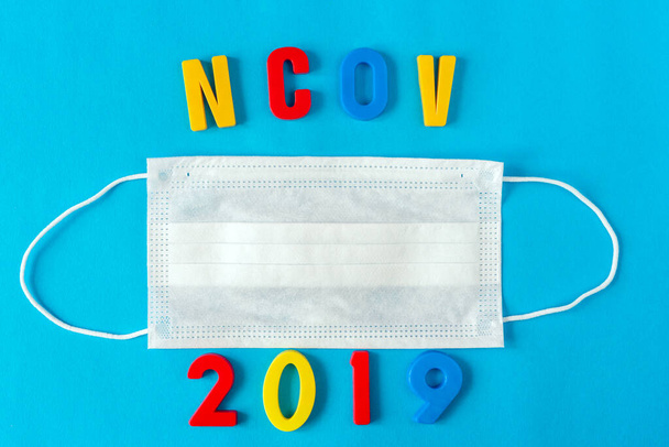 Medizinische Atemschutzmaske zum Schutz vor Viren auf blauem Hintergrund mit der Aufschrift ncov 2019. - Foto, Bild