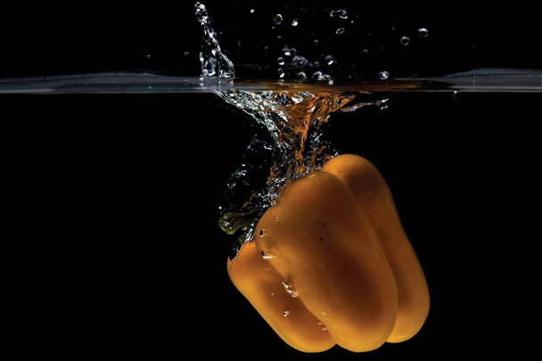 Close up view of colorful yellow pepper falling in water on black background.  Gorgeous backgrounds. - Photo, Image