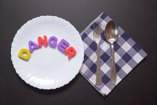 Kolorowe litery ze słowem niebezpieczeństwo na talerzu z widelcem i nożem, dodatek do żywności i niezdrowej koncepcji żywności. - Zdjęcie, obraz