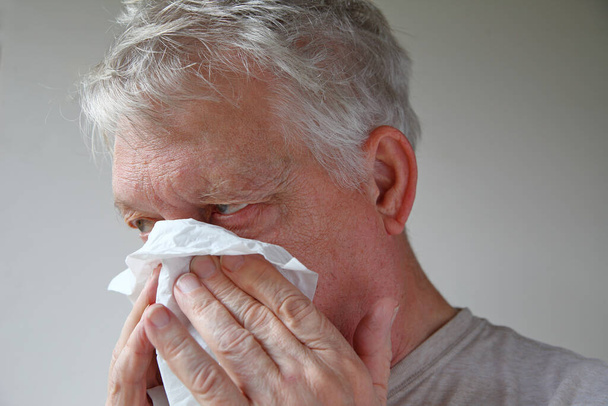 Met een zakdoekje blaast een oudere man zijn neus met ruimte voor tekst. - Foto, afbeelding