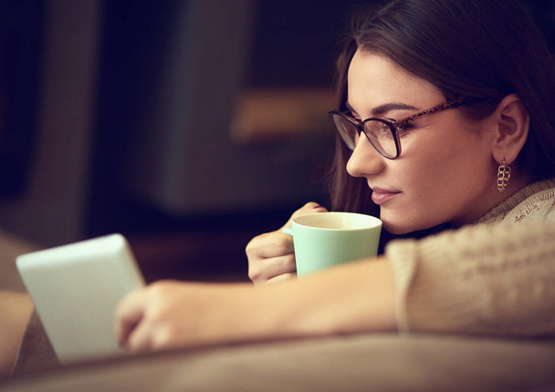 Mujer sentada en la alfombra cerca del sofá usando una tableta, bebiendo café de una taza. Concepto de educación en línea
. - Foto, imagen