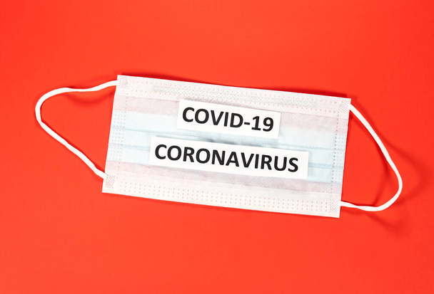 Coronavirus COVID-19 escribiendo sobre una máscara blanca sobre fondo rojo. Un nuevo coronavirus es un nuevo coronavirus que no ha sido identificado previamente. El virus que causa la enfermedad coronavirus COVID-19
 - Foto, imagen