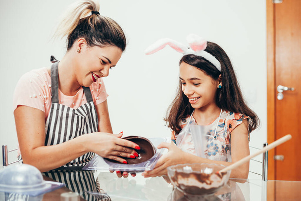 Mother and daughter making homemade chocolate easter eggs. Easter in Brazil. - Foto, Imagen