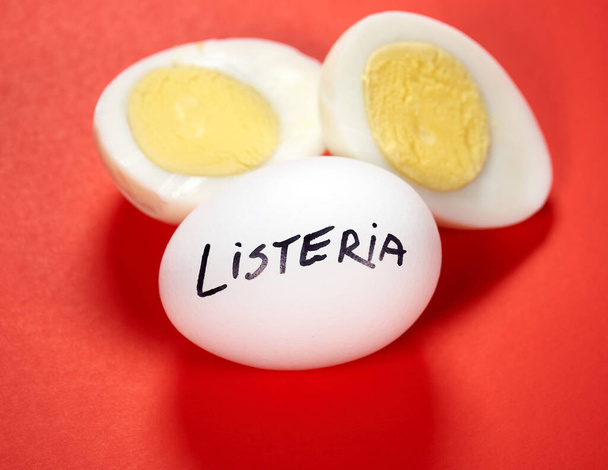 Huevo duro con Listeria escribiendo sobre el huevo sobre fondo rojo. La listeriosis es una infección transmitida por alimentos causada por la bacteria Listeria. La listeria es causada por bacterias que pueden crecer a temperaturas frías
 - Foto, imagen