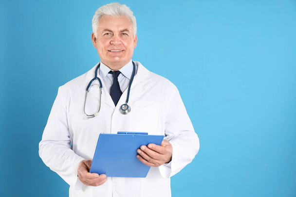 Portrait of senior doctor with clipboard against blue background, space for text - Фото, зображення