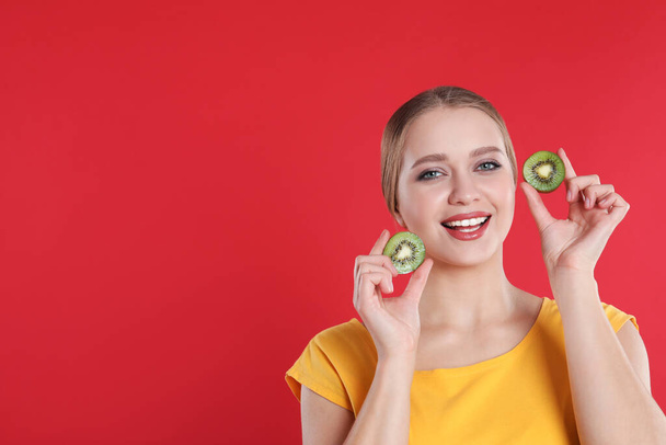 Young woman with cut kiwi on red background, space for text. Vitamin rich food - Fotoğraf, Görsel