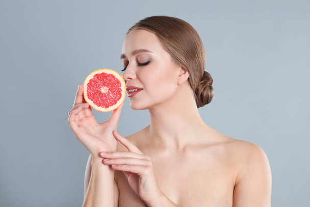 Young woman with cut grapefruit on grey background. Vitamin rich food - Fotó, kép
