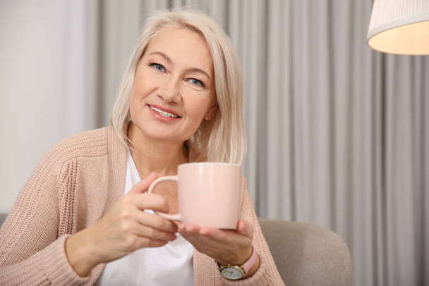 Beautiful mature woman with cup of coffee at home. Space for text - Foto, afbeelding