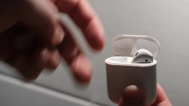 Mans hand puts airpods in a box. Concept. Man puts the airpods headphones in the box for charging - Footage, Video