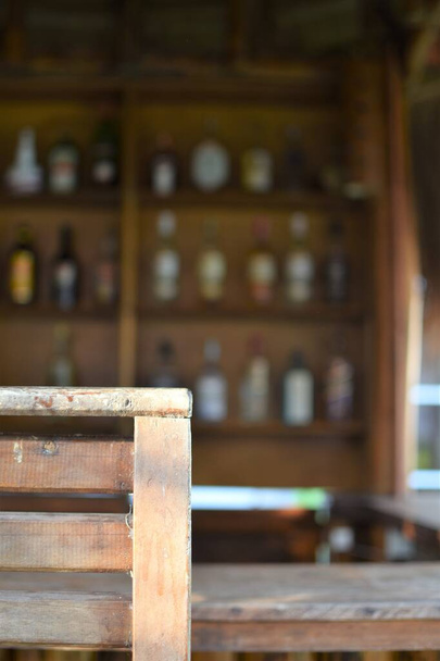Pusty drewniany stołek w barze na świeżym powietrzu z rzędami butelek z alkoholem w tle - Zdjęcie, obraz