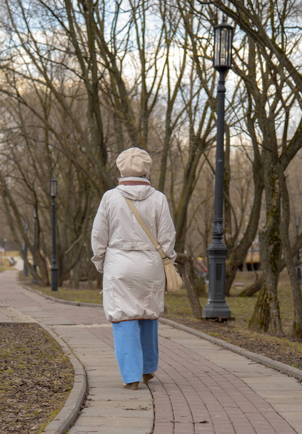 An elderly , elegantly dressed woman walks along an alley in a public Park in early spring. - Fotó, kép