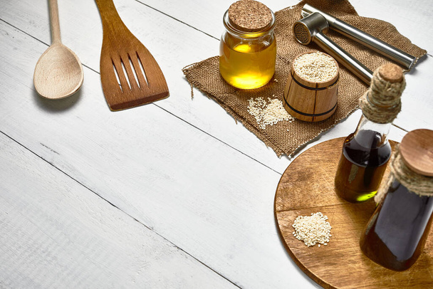 sesame seed in wooden bowl on the table and garlic pressing masher, Cold pressed oil in glass jar and bottle on the background of wooden boards - 写真・画像