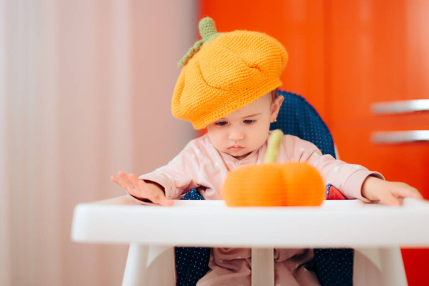 Baby Girl Playing with Knitted Pumpkin Toy Wearing Funny Hat - 写真・画像