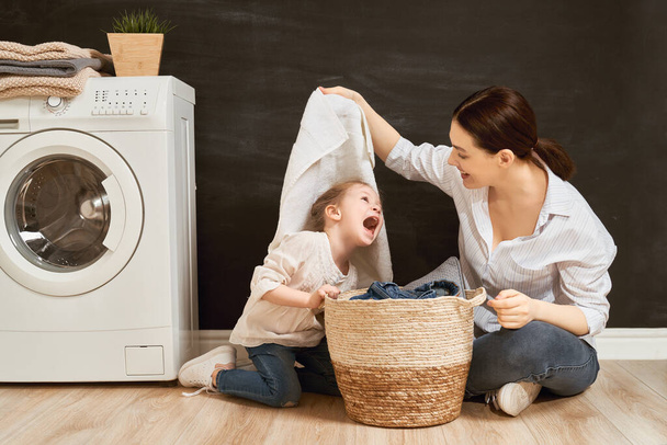 Krásná mladá žena a dítě dívka malý pomocník se baví a usmívá se při praní prádla doma.                                - Fotografie, Obrázek