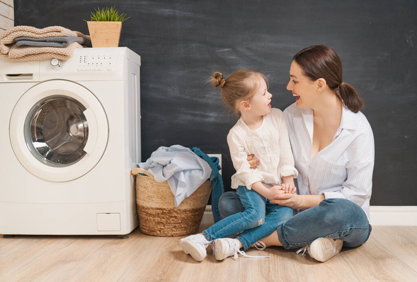 Beautiful young woman and child girl little helper are having fun and smiling while doing laundry at home.                                - Foto, Imagen